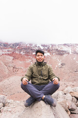 Poster - Vertical shot of the young man in the mountains, sitting on the rock and meditating.