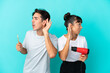 © luismolinero - Young mixed race couple holding a hairdryer and toothbrush isolated on blue background listening to something by putting hand on the ear