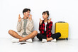 © luismolinero - Young mixed race travelers couple sitting on the floor isolated on white background with fingers crossing and wishing the best