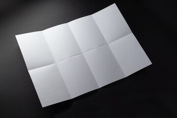 Light and shadow on creases in sheet of white paper folded into eight equal sections, on black