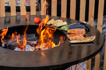 Process of cooking meat steaks, zucchini, eggplant, tomato on grill, brazier at outdoor summer local food market - close up. Gastronomy, cookery and street food concept