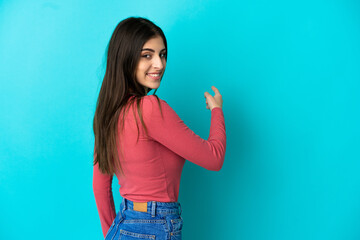 Young caucasian woman isolated on blue background pointing back