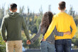 Woman holding hands with another man while hugging her boyfriend outdoors on sunny day, back view. Love triangle