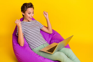 Poster - Photo of celebrate millennial lady sit on bag work laptop yell wear t-shirt jeans isolated on yellow background