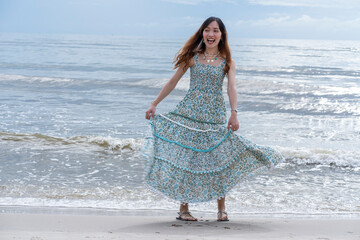 Asian girl wearing a dress, walking, spinning skirt, relaxing, happy to go on a summer vacation at the sea beach. 