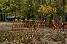 Wooden Furniture Of A Street Cafe Standing In The Park And Fallen Dry Yellow Leaves Lying Around The Furniture.