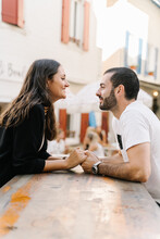 Loving Young Ethnic Couple Smiling And Holding Hands In Outdoor Cafe