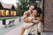 © LIGHTFIELD STUDIOS - happy man embracing excited african american girlfriend near building outdoors.