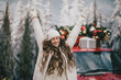 © polinaloves - Happy beautiful woman wearing knitted sweater and woolen hat standing near red car with Christmas tree on the top under snowfall.