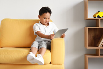 Sticker - Little African-American boy with tablet computer watching cartoons on armchair at home