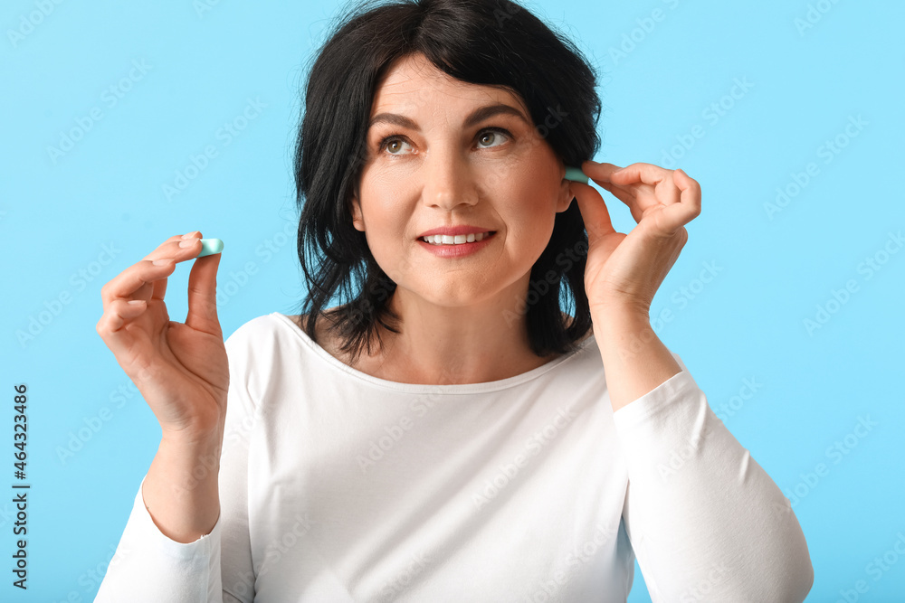 Mature woman putting ear plugs on blue background