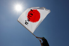 青空と太陽の下で頑張れ日本と書かれた旗を振る男性