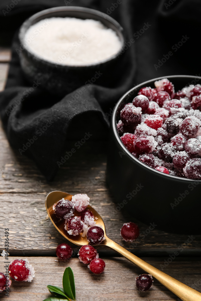 Bowl and spoon with tasty sugared cranberries on wooden background
