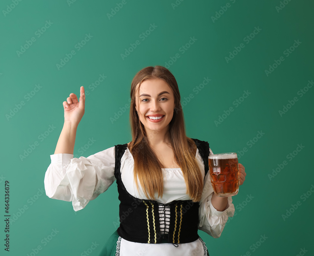 Beautiful Octoberfest waitress with pale beer pointing at something on green background