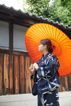 日本家屋の横を、和傘をさして歩く浴衣の女性