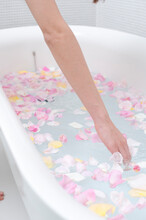 薔薇の花弁が浮かぶバスタブの湯と女性の手