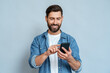 Smiling European business man using smartphone device looking at mobile phone screen scrolling enjoying communication with friends. Handsome businessman holding cellphone isolated on blue background