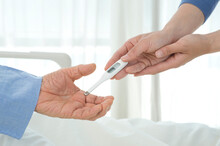 病院のベッドの患者に体温計を渡す看護師の手