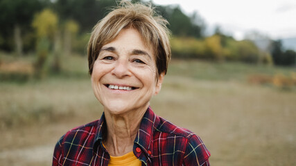 Happy senior woman smiling on camera outdoor in the woods - Focus on eyes