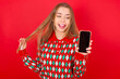 Photo of nice pretty Young beautiful caucasian girl wearing christmas sweaters on red background demonstrate phone screen hold hair tails