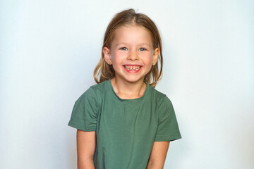 portrait of a happy child on a white background in a green t-shirt smiling. The little girl plays with her sly eyes. Happy girl. copy space. Childhood concept.