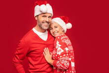 Loving Mature Couple In Santa Hats Hugging And Smiling Heartily For The Camera.