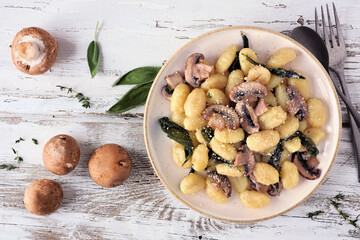 Sticker - Gnocchi with mushrooms in a brown butter sage sauce. Top view table scene on a rustic white wood background.
