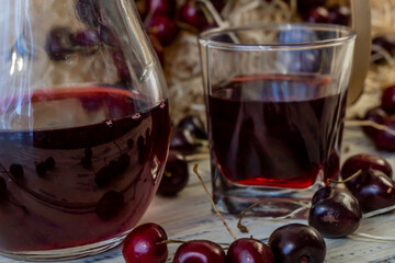 Cherry and cherry juice or wine on a wooden table, a decanter and a glass with juice, a basket with cherries