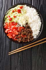 Wall Mural - Takoraisu dish consists of ground beef, cheese, lettuce, and tomatoes served on a bed of short grain rice close-up in a bowl on the table. vertical top view from above