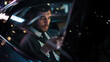 © Gorodenkoff - Handsome Businessman in a Suit Commuting from Office in a Backseat of His Luxury Car at Night. Entrepreneur Using Smartphone while in Transfer Taxi in Urban City Street with Working Neon Signs.
