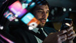 © Gorodenkoff - Handsome Businessman in a Suit Commuting from Office in a Backseat of His Car at Night. Entrepreneur Using Smartphone while in Transfer Taxi in Urban City Street with Working Neon Signs.
