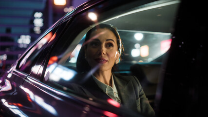 Wall Mural - Beautiful Businesswoman is Commuting from Office in a Backseat of Her Luxury Car at Night. Entrepreneur Passenger Traveling in a Transfer Taxi in Urban City Street with Working Neon Signs.