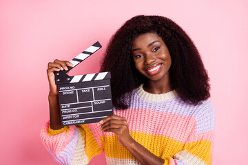 Poster - Photo of attractive cheerful dark skin person hands hold clapboard look camera isolated on pink color background