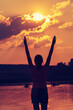 Silhouette of a young woman with arms raised in the backdrop of the setting sun