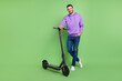 © deagreez - Full length photo of young cheerful man happy positive smile walk electric scooter isolated over green color background