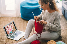 Young Woman Knitting Wool Using Needle While Watching Online Tutorial On Laptop At Home. Woman Watching Needlework Lessons, A Laptop And Home Hobbies. Caucasian Woman Learning To Knit Online