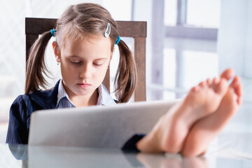 Wall Mural - Humorous portrait of business child girl with bare feet on the table is happy to return to work in office after lockdown. Selective focus. Horizontal image.