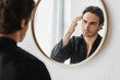 © LIGHTFIELD STUDIOS - Blurred man in silk robe touching hair while looking at mirror in bathroom
