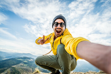 Wall Mural - Young hiker man taking selfie portrait on the top of mountain - Happy guy smiling at camera - Hiking and climbing cliff
