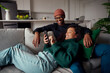 Multi-ethnic couple laughing, looking at text on phone while on the couch in modern apartment
