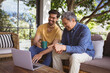 © Wavebreak Media - Smiling biracial adult son and senior father using laptop and drinking coffee in garden