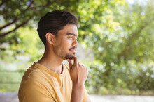 Smiling Biracial Man Touching His Chin And Thinking In Garden