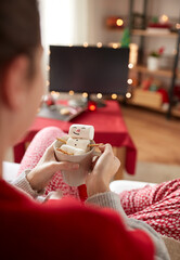 Wall Mural - christmas, winter holidays and leisure concept - close up of hands holding mug with marshmallow snowman at home