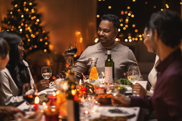 Wall Mural - holidays, party and celebration concept - multiethnic group of happy friends having christmas dinner at home and drinking wine