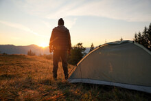Man Near Camping Tent In Mountains At Sunset, Back View