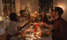 Holidays And Celebration Concept - Multiethnic Group Of Happy Friends With Sparklers Having Christmas Dinner At Home