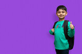 Fototapeta Sport - Happy smiling boy with thumb up is going to school. Child with school bag and books. Kid indoors on a background. Back to school.