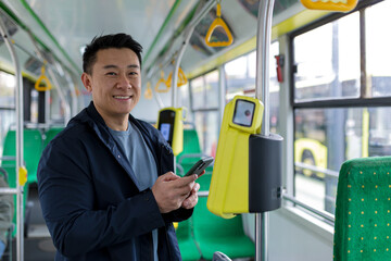 Happy and successful asian male passenger in public transport bought a ticket using a mobile phone smiling and looking at the camera