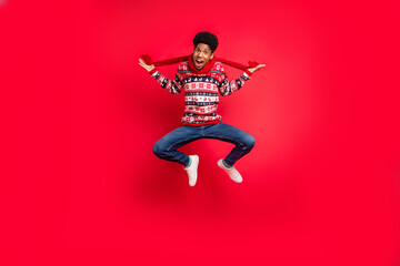 Wall Mural - Full body photo of young afro guy happy positive smile jump up scarf winter holiday isolated over red color background