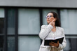 © LIGHTFIELD STUDIOS - african american businesswoman with notebook looking away while adjusting earphone on city street